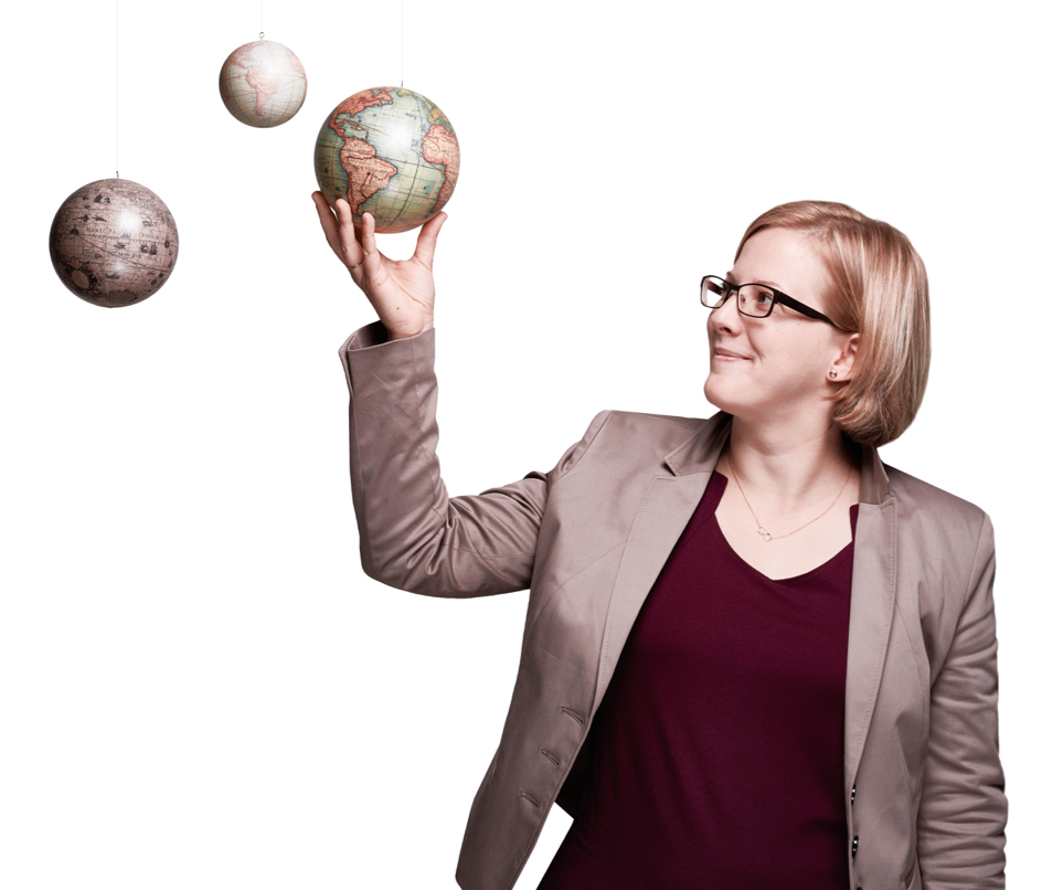 Ms. Antos holds a suspended globe in her hand and smiles